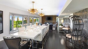 Un espace de salle à manger moderne avec une longue table blanche, des chaises noires et blanches, et un luminaire au plafond au design original.