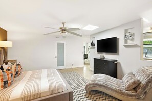Un dormitorio moderno con cama, sofá, televisión, ventilador de techo y ventana.