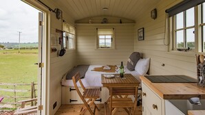 Una cabaña acogedora con cama, una mesa de madera y sillas, una ventana pequeña y vistas al campo.
