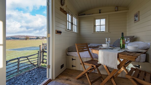 Una habitación acogedora con una mesa de madera dispuesta para comer, una cama con almohadas y vistas a un campo cubierto de hierba por la ventana.