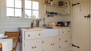 Una cocina con una mesa de madera, un lavamanos y armarios. Hay estantes sobre la encimera con diversos utensilios de cocina.