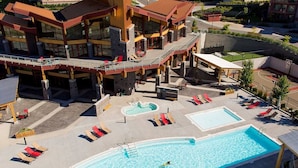 Een hotel met een groot buitenzwembad, meerdere loungegedeeltes met ligbedden en een overdekt terras.