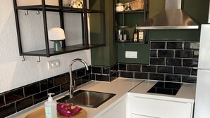 Eine Küche mit weißer Arbeitsplatte, Spüle aus Edelstahl, schwarzer Spritzschutzwand und Kühlschrank in Weiß.