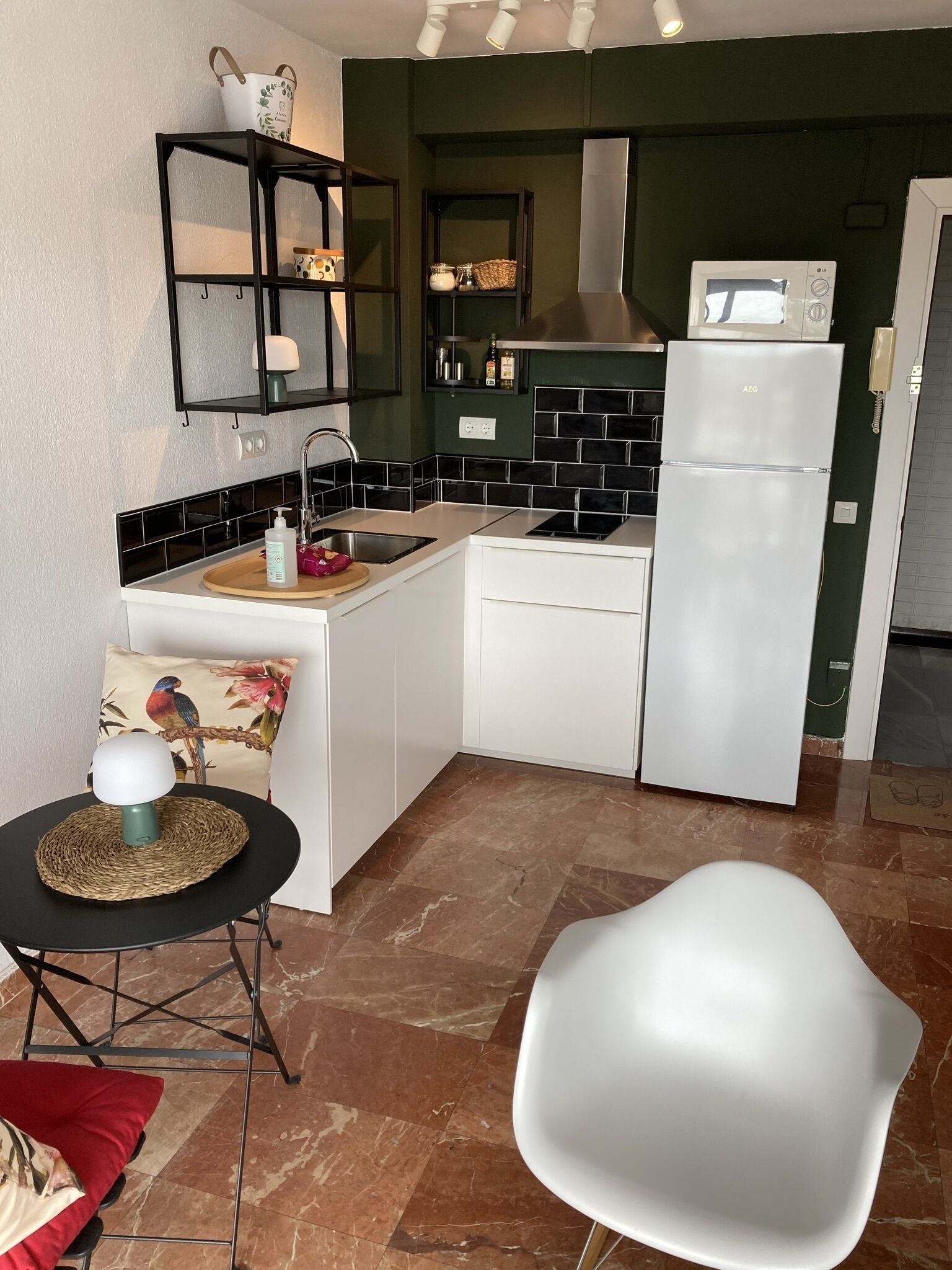 Una cocina compacta con un refrigerador blanco, un lavamanos y una pequeña zona de comedor con una mesa y una silla.
