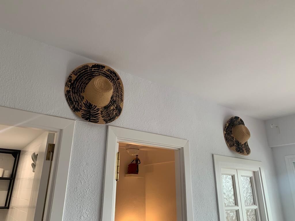A hallway with two hats hanging on the wall, a door leading to a room, and a small statue on the left.