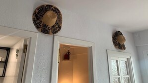 Ein Flur mit zwei an der Wand hängenden Hüten, einer zur Kammer führenden Tür und einer kleinen Statue links.
