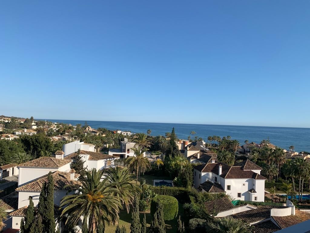 Uma área residencial costeira com edifícios brancos, palmeiras e vista para o mar.