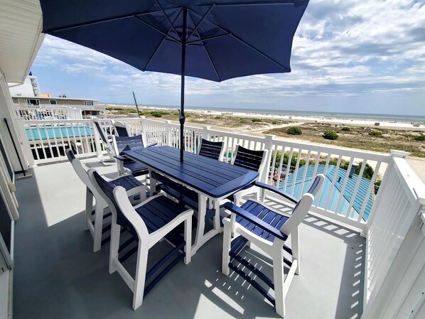 A deck with a table and chairs, a pool, and a view of the beach. - 4br Beachfront Condo with Ocean Views and Pool (Wildwood Crest)