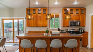 A modern kitchen with wooden cabinets, a central island with bar stools, a microwave, and a stove.