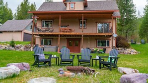 A two-story house with a porch, four Adirondack chairs, and a fire pit.