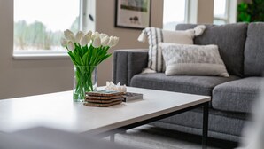 A modern living room with a grey sofa, a coffee table with a vase of white tulips, and a framed picture on the wall.