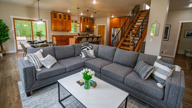 A modern living room with a gray sectional sofa, a white coffee table, and a kitchen in the background.