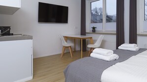 Ein modernes Hotelzimmer mit Bett, Schreibtisch, Stuhl, Fernseher und einem Fenster mit Vorhängen.