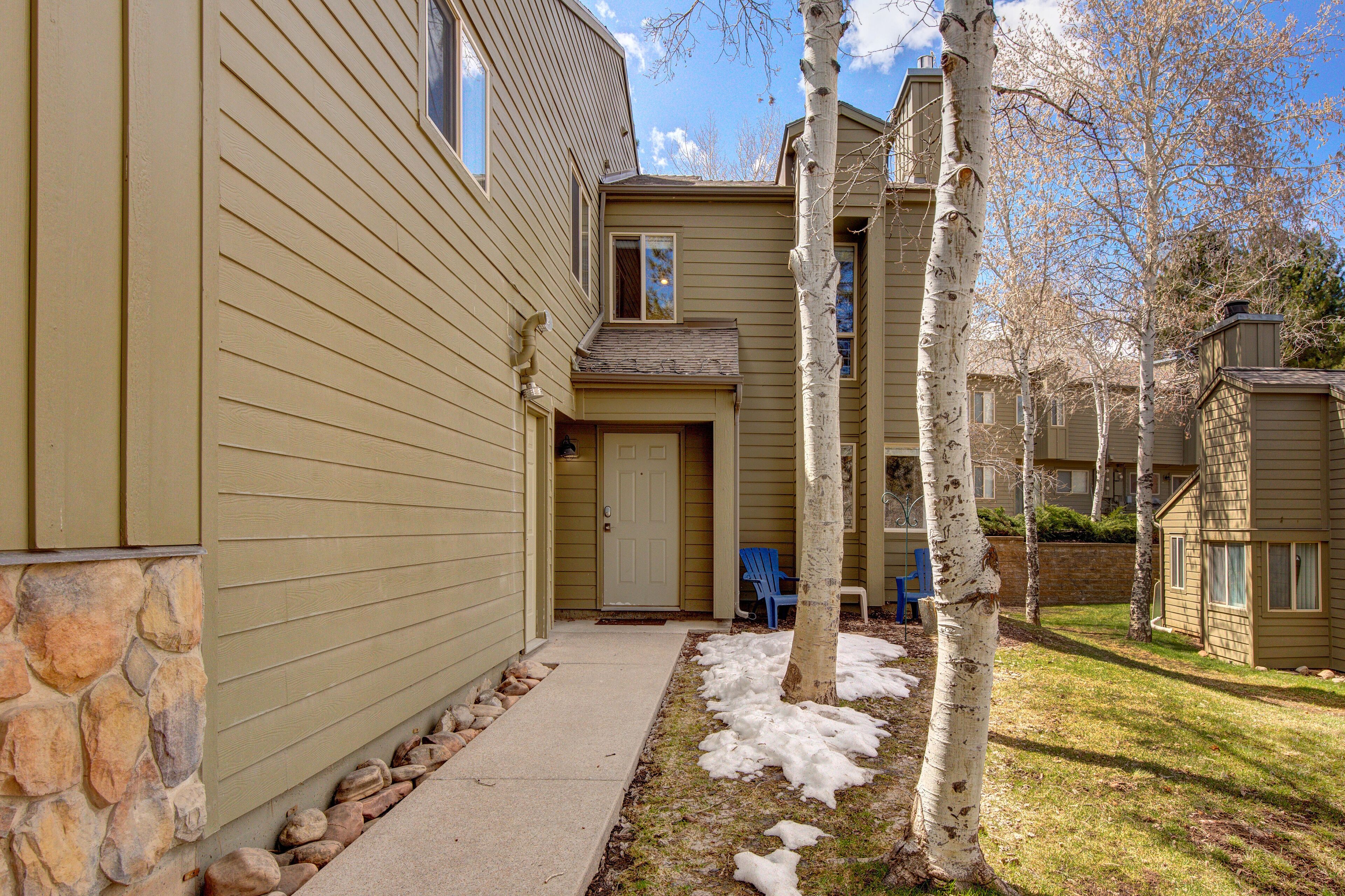 A two-story building with a stone foundation and siding, a front door, and a blue chair outside.