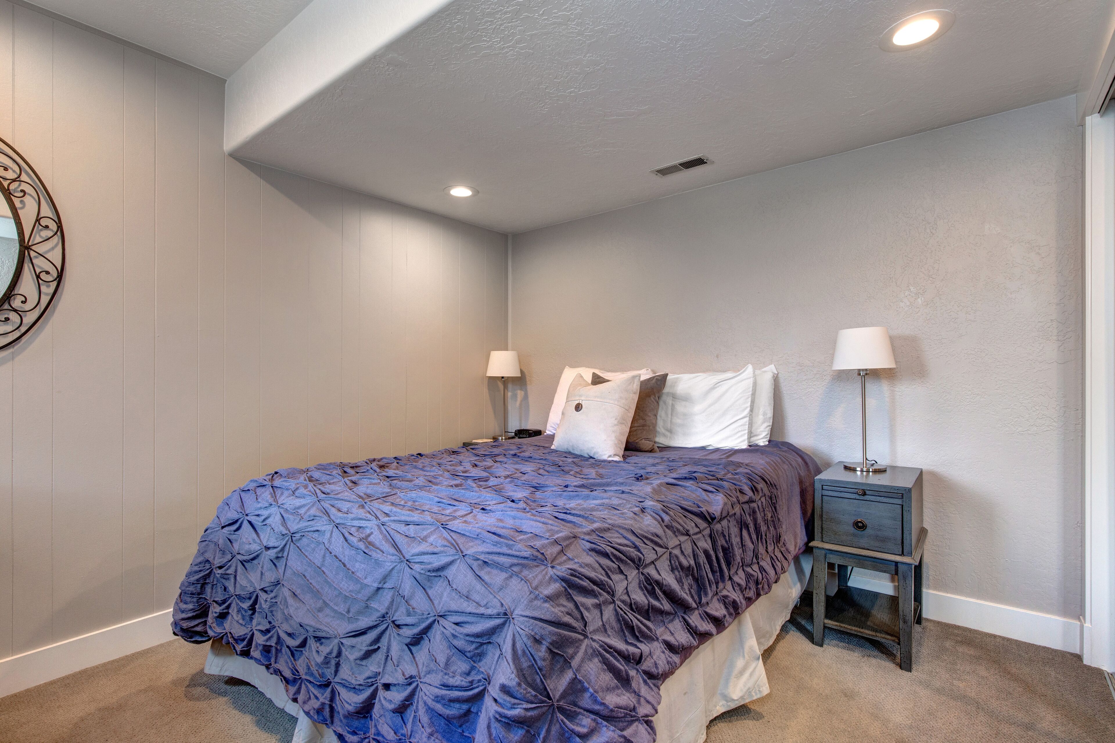 A bedroom with a bed, two bedside tables, and a wall-mounted light fixture.