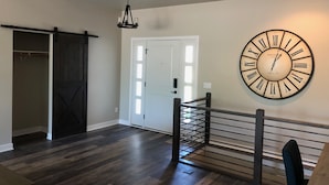 Una habitación amplia con un reloj de pared grande, una puerta corredera estilo granero y una escalera con barandilla metálica.