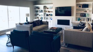 Una sala de estar moderna con chimenea, un televisor de pantalla plana grande y una estantería llena de objetos decorativos.