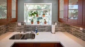 Una cocina con un lavamanos doble, una ventana con plantas en macetas y un salpicadero de azulejos.