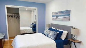 Un dormitorio con cama, mesita de noche, lámpara y un cuadro en la pared.