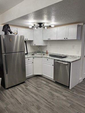 A modern kitchen with white cabinets, a stainless steel refrigerator, and a granite countertop.