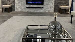 Un salon moderne avec un téléviseur à écran plat fixé à un mur en pierre, une table basse en verre avec des télécommandes et un lustre.