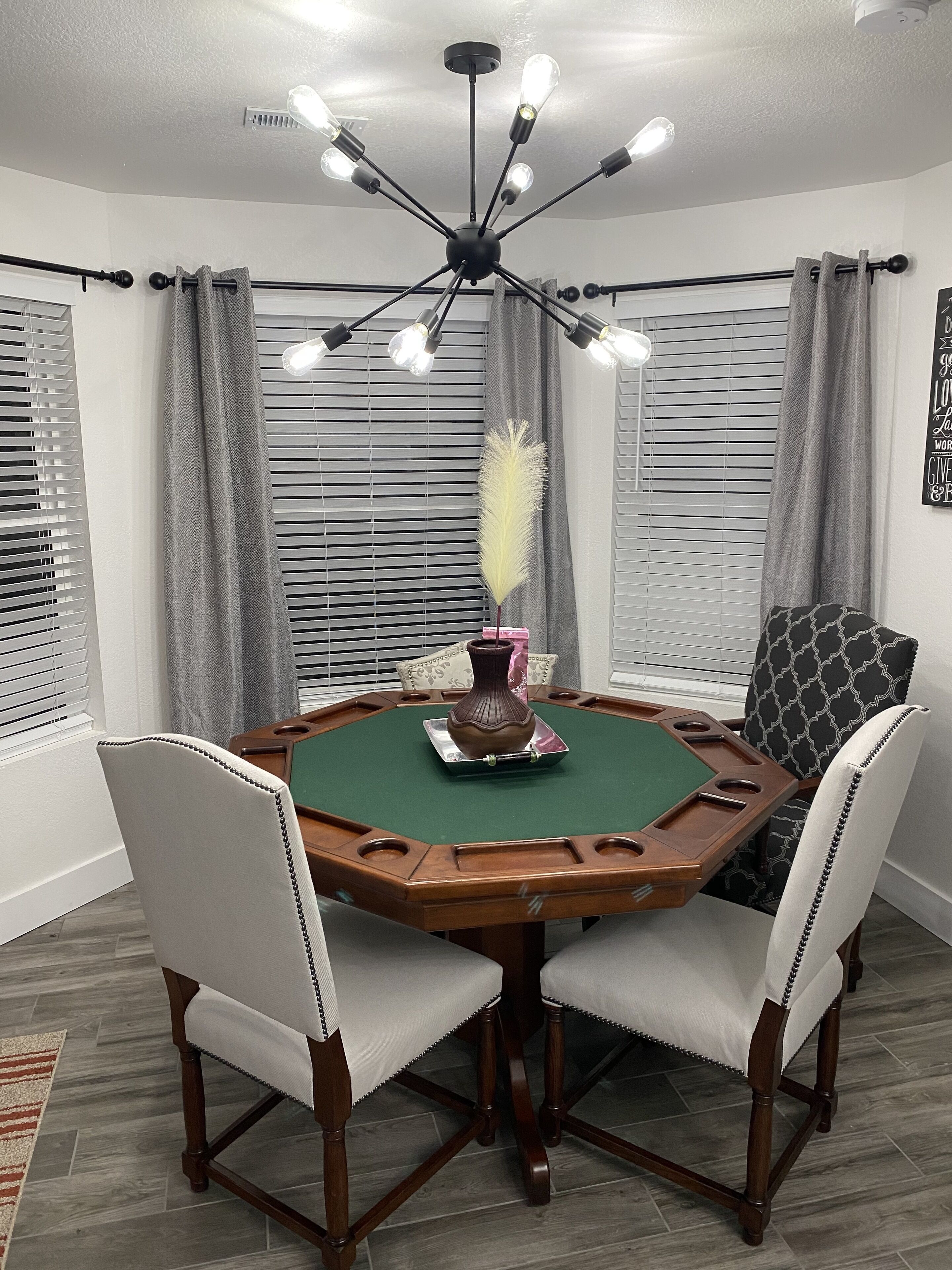 A room with a green felt table, wooden chairs, a vase, and a ceiling light fixture.