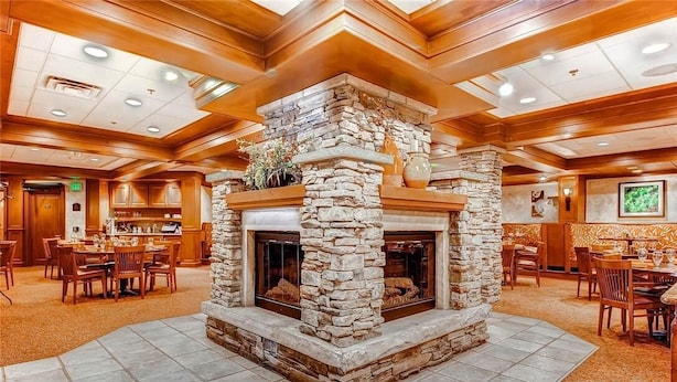 Eine geräumige Lobby mit Kamin aus Stein, Holzboden und mehreren Essbereichen.