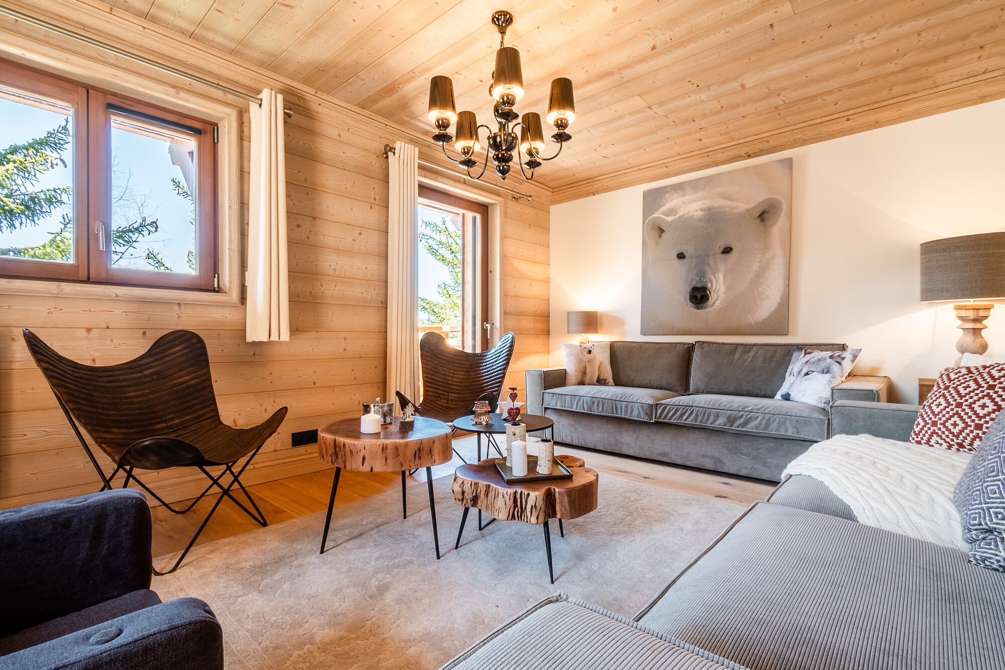 Un salon chaleureux aux murs en bois, orné d’une grande œuvre d’art sur le thème des ours et agrémenté d’un lustre moderne.