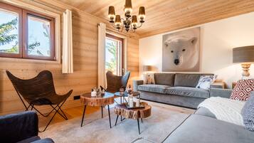 Un salon chaleureux aux murs en bois, orné d’une grande œuvre d’art sur le thème des ours et agrémenté d’un lustre moderne.