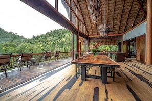 A wooden deck with a dining table and chairs, overlooking a lush green landscape.