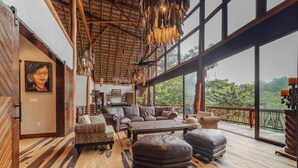 A spacious living area with a large sofa set, a dining table, and a view of lush greenery through large windows. - Valley Stream Private Eden (St. Margaret's Village)