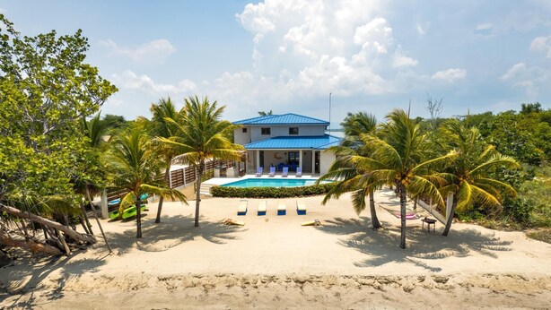 Een strandpand met een zwembad, palmbomen en een gebouw met een blauw dak.
