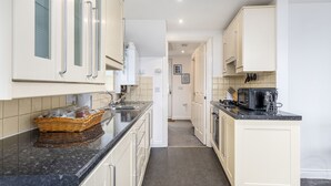 A narrow kitchen with white cabinets, a black countertop, and a central island. - Liquorice Suite (Lincoln)