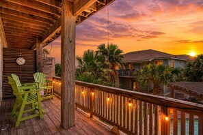 Una terrazza in legno con sedie, un orologio e luci a stringa sullo sfondo di un tramonto.