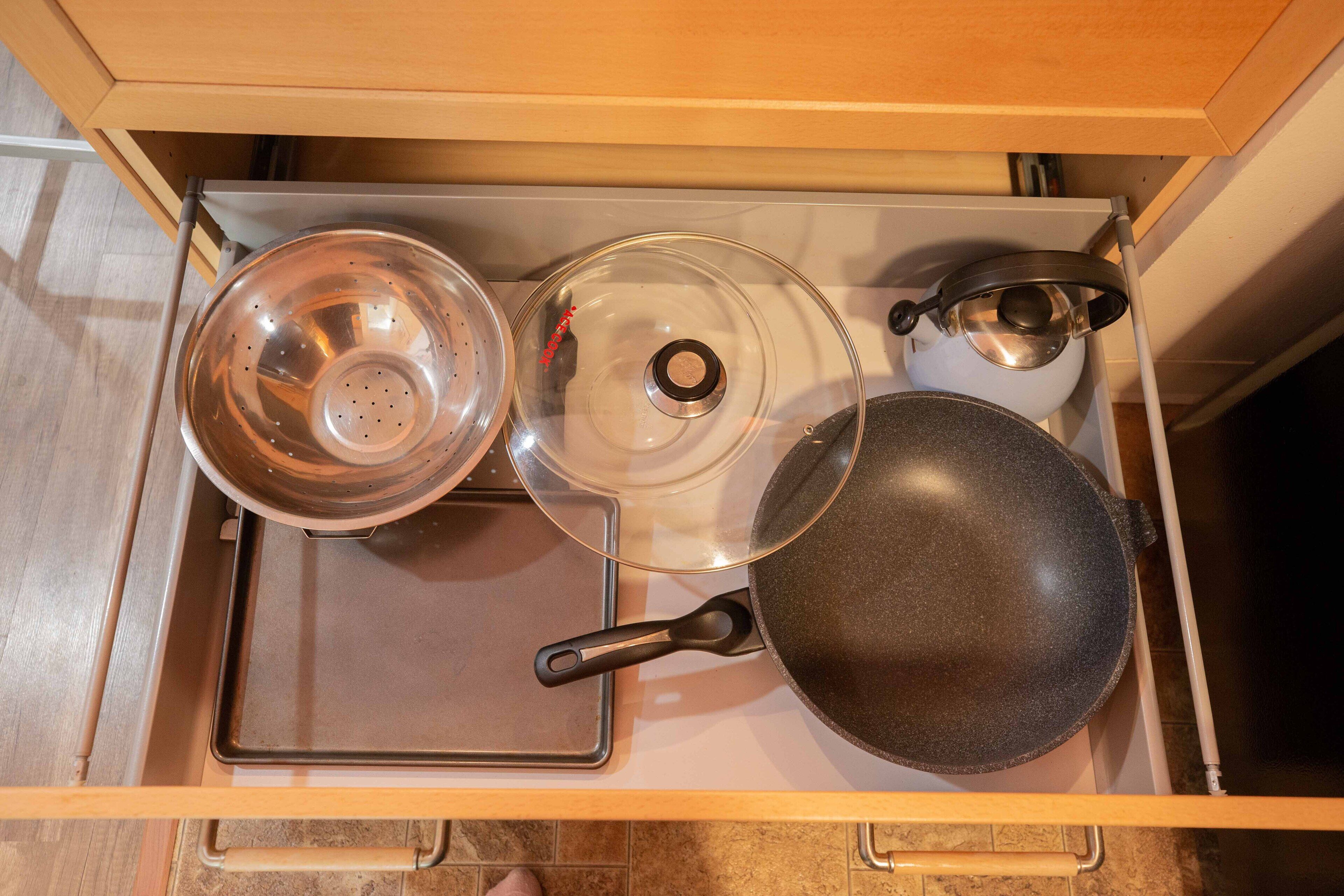 Uma gaveta de cozinha com um fogão, uma frigideira, uma panela e um escorredor.