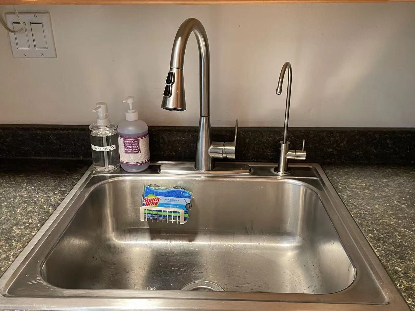 Ein Spülbecken aus Edelstahl mit einem modernen Wasserhahn, einer Seifenspender und Geschirrspülmittel.