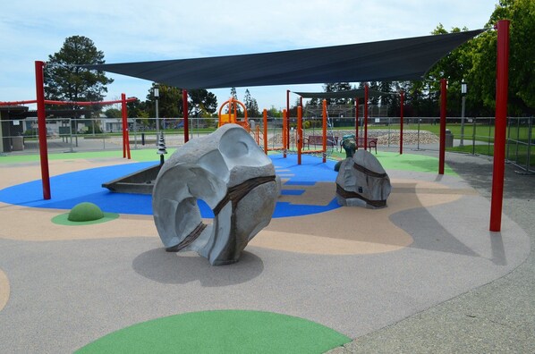 A playground with climbing structures, a shaded area, and a large rock sculpture.