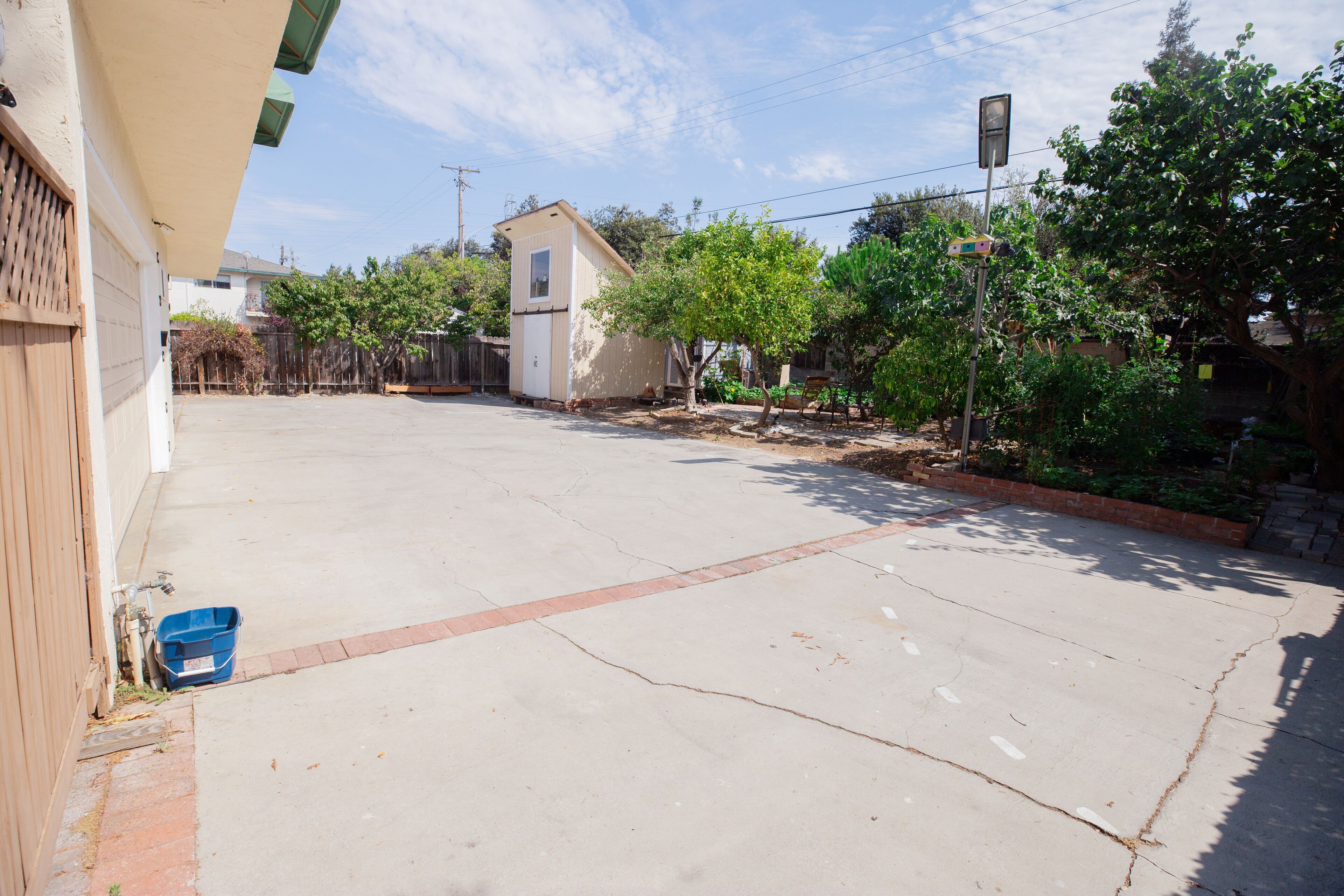 Una calle residencial con un garaje, un cobertizo pequeño y un camino bordeado de árboles.