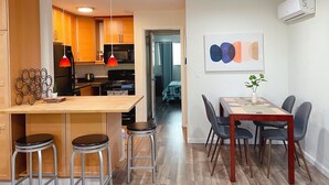 A modern kitchen with wooden cabinets, a black refrigerator, and a red pendant light. There is a dining area with a wooden table, four chairs, and a vase with a plant. - 💎Cozy 1B/1B in a prime location • 🌲AC/ 1000mb wifi/ Washer, dryer/ more… (Sunnyvale)