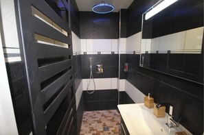 Bathroom features a sleek design with a black and white tiled wall, a sink, and a handheld showerhead.