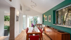 A dining area with a wooden table and red chairs, a wooden cabinet, and a green wall with a window. - Luxury Suite Jasmin-Two Bedroom Suite with Hot Tub (Split)