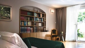 A bedroom with a large bookshelf, a bed with a green blanket, a chair, and a window with curtains. - Luxury Suite Jasmin-Two Bedroom Suite with Hot Tub (Split)