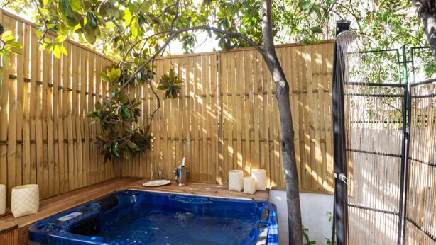 A hot tub with a wooden deck, surrounded by a bamboo fence and a tree. - Luxury Suite Jasmin-Two Bedroom Suite with Hot Tub (Split)