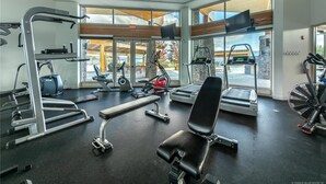 Un gimnasio con diversos equipos de ejercicio, ventanas amplias y vistas al exterior.
