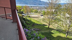 Un balcón con vistas a un jardín ajardinado, una masa de agua y montañas distantes.