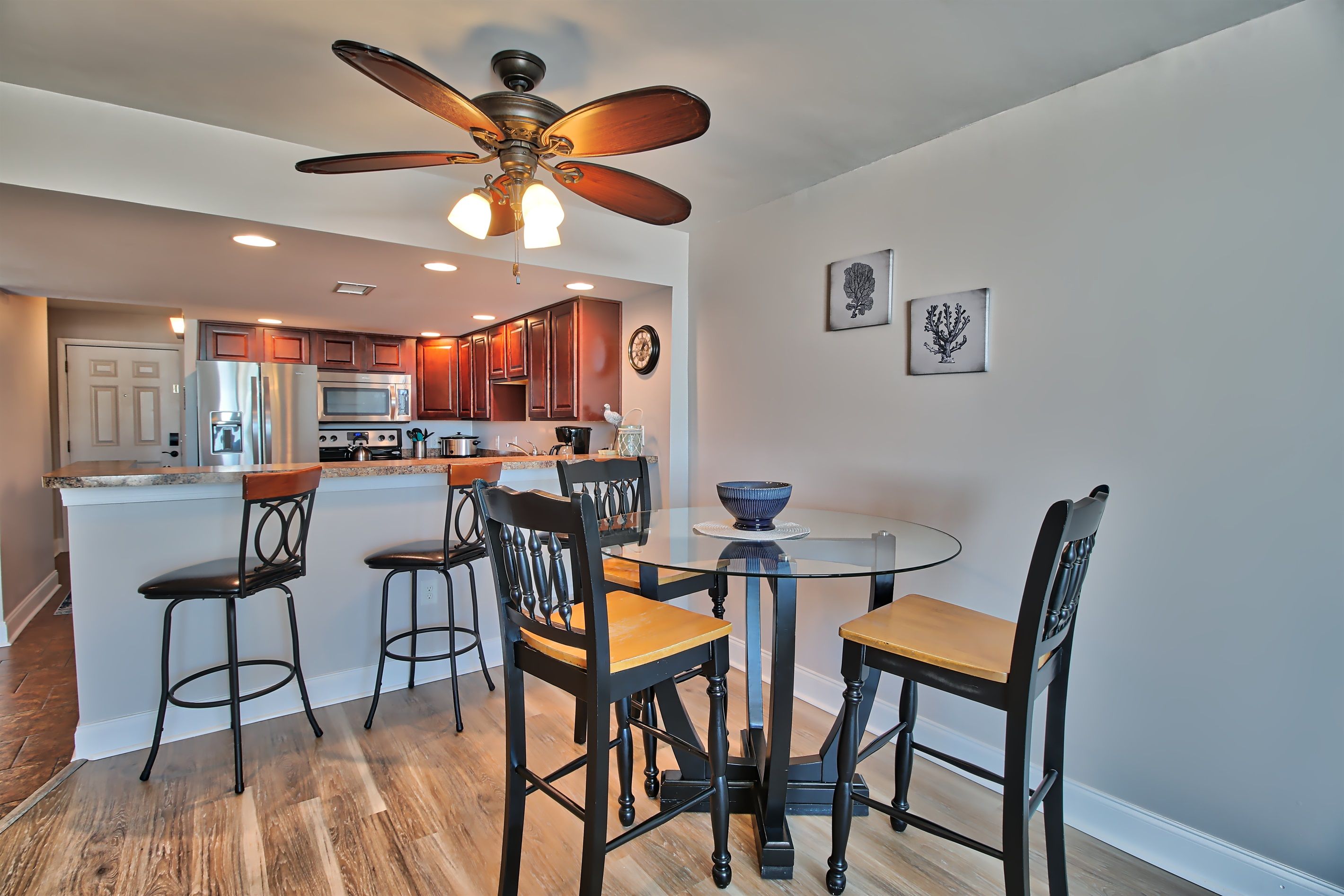 A modern kitchen with a central island, bar stools, and a ceiling fan.