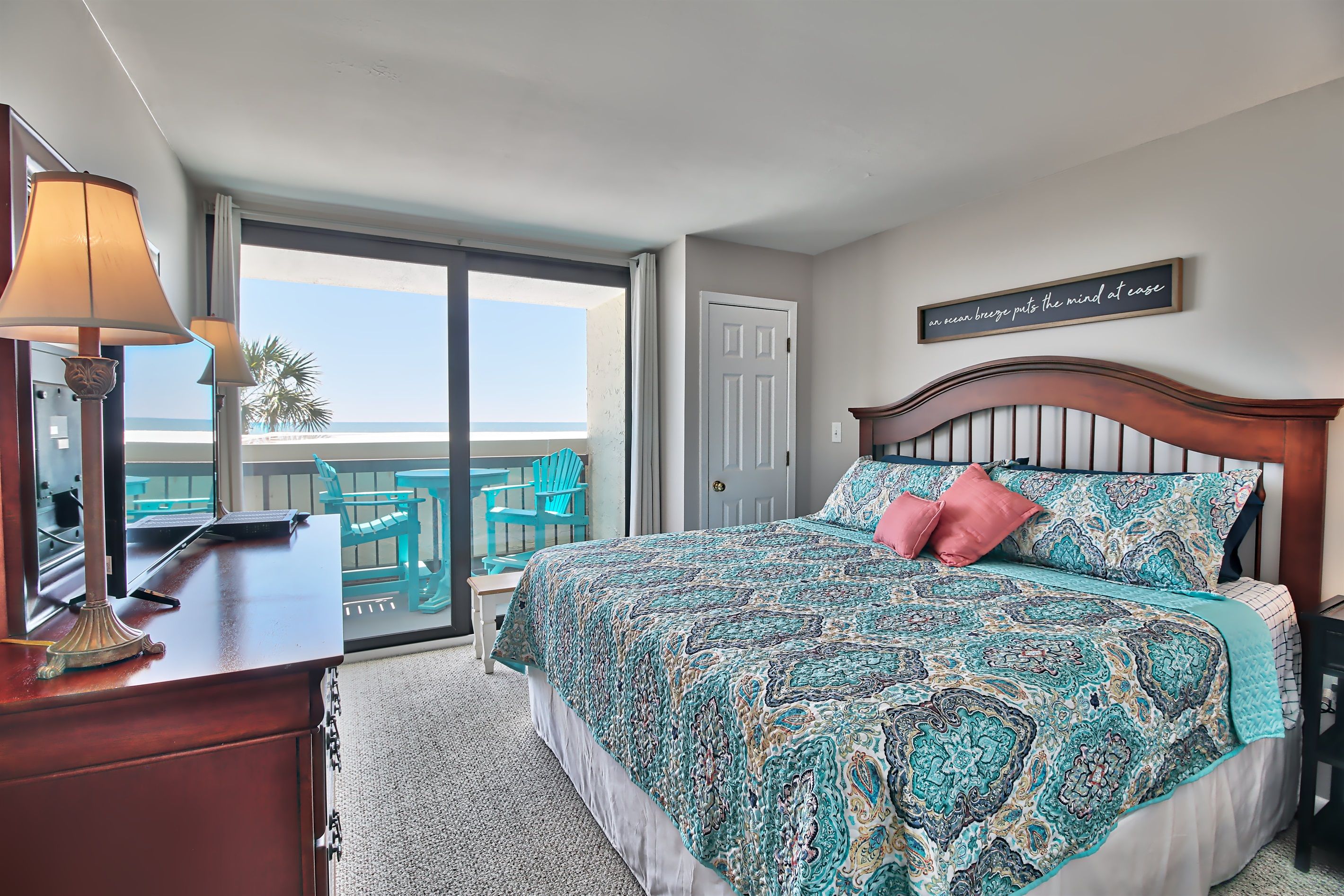 A bedroom with a large bed, a desk with a lamp, a view of the balcony, and a sign on the wall.