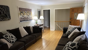 A living room with a dark brown sofa set, a wooden floor, a painting on the wall, and a door with a mirror. - Suburb in the City (Atlanta)