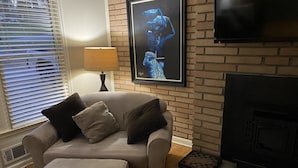 A living room with a beige sofa, a matching ottoman, a fireplace, and a framed artwork on the wall. - Suburb in the City (Atlanta)