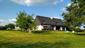 Una casa con un amplio jardín, zona de estar al aire libre y un porche cubierto.